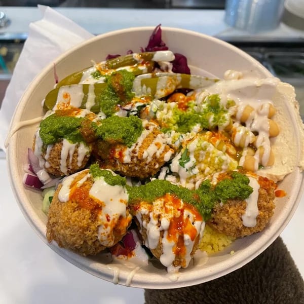 A close-up of a Moshe's falafel bowl, topped with green sauce, white sauce, and red sauce.