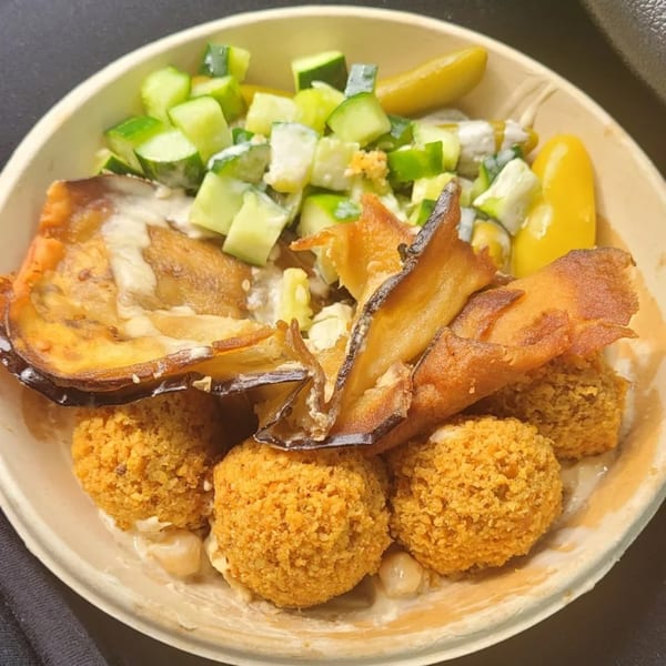 Moshe's falafel bowl with crispy falafel, fried eggplant, cucumber salad, and pickles.