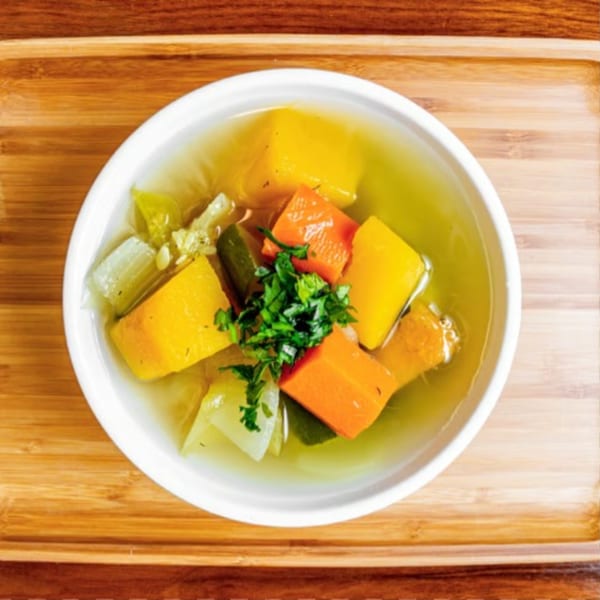 Overhead view of a white bowl filled with clear vegetable soup, garnished with parsley.