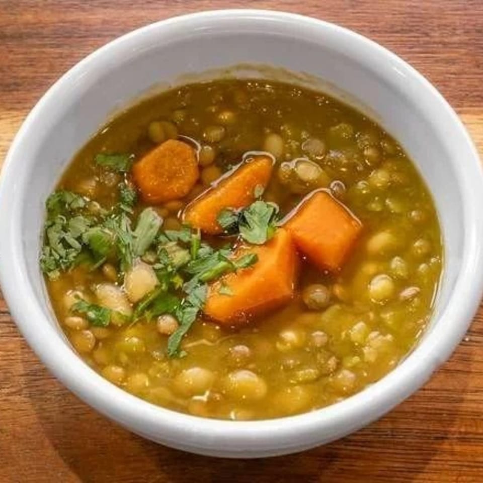 Hearty kosher lentil soup with carrots and fresh cilantro in a white bowl on a wooden table.