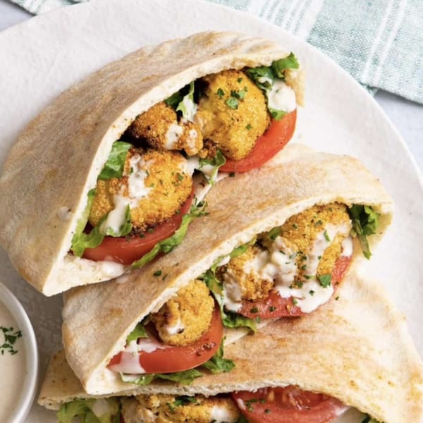 Three Moshe's falafel pita sandwiches filled with crispy falafel, lettuce, tomatoes, and tahini sauce.