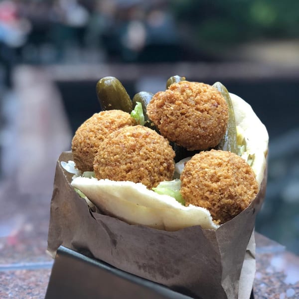 Moshe's falafel pita with crispy falafel balls, lettuce, and pickles in a brown paper wrap.